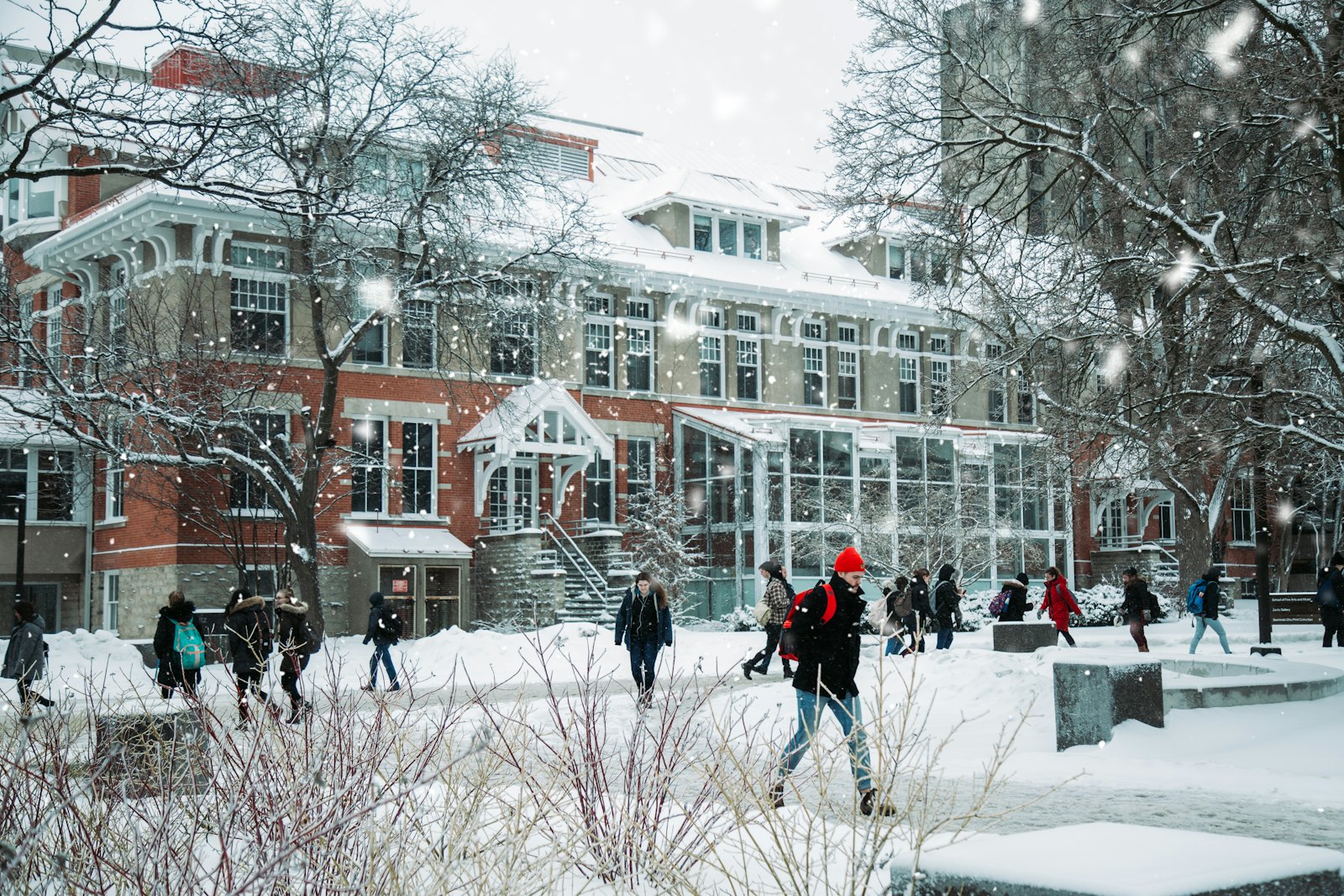 冬日雪天,穿着厚重冬装的学生们走过一座砖红色的学校建筑前,雪花纷飞